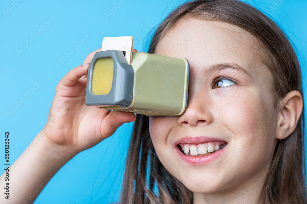 Smiling child girl looks at old photos through a diascope. Banner template on blue background.