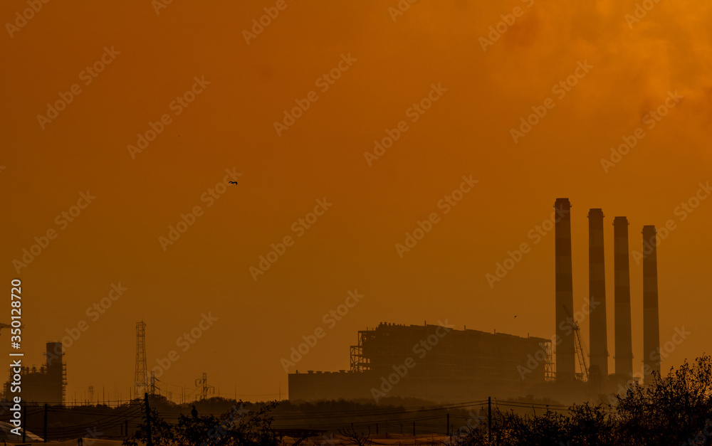 Power plant with orange sunset sky and birds flying on the sky. Air pollution concept. Energy for support factory in industrial estate. Power and energy. Dust spread in the air in the evening.