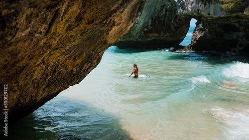 Surfer entering water in Suluban surfing spot. Bali, Indonesia. On vacation during a sunny day, with an intense blue sky and big rocks break on background. Surfer holding copy-space surfboard