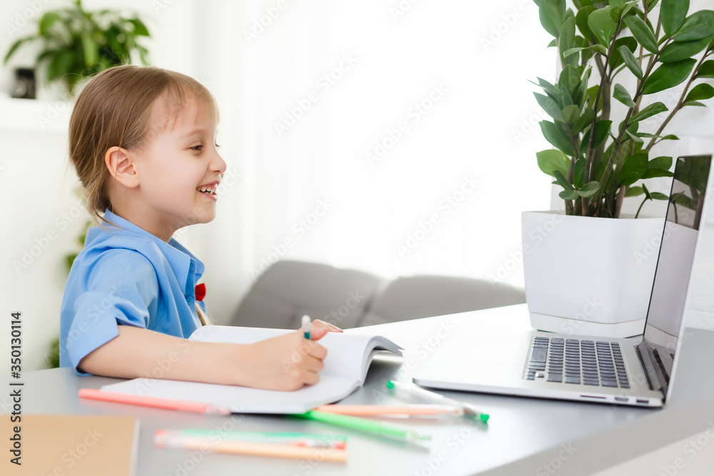 Cute little girl is sitting at table with her laptop and studying online Cute little girl is sitting at table with her laptop and studying online