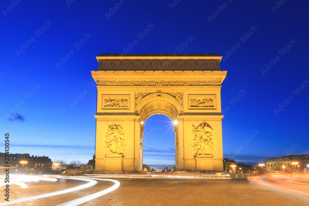Beautiful cityscape urban street view of the Arc de Triomphe in Paris, France, on a spring evening after sunset in the blue hour, seen from the Champs-Elysees with traffic