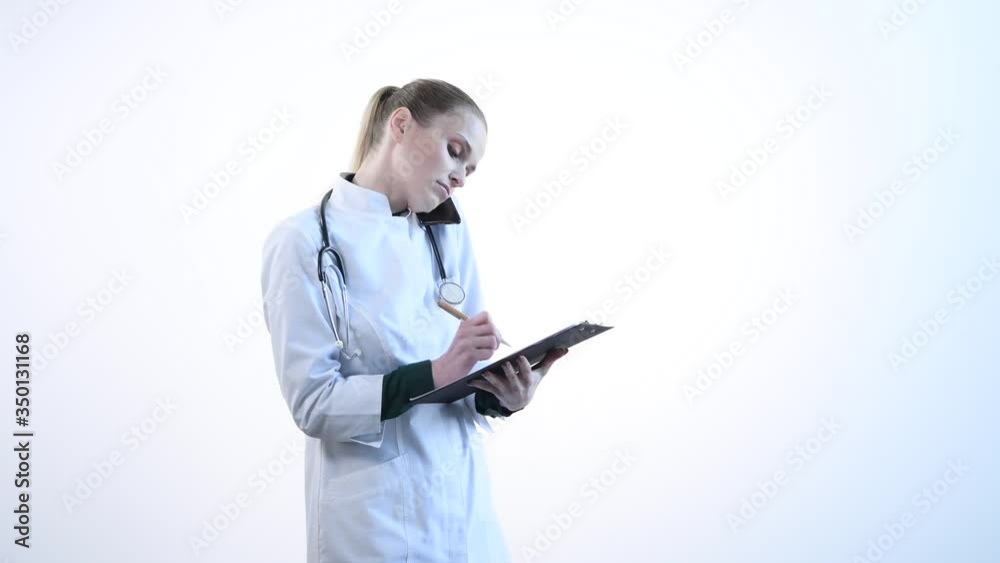 A young female doctor talks on the phone and records the information in the clipboard. A young female doctor talks on the phone and records the information in the clipboard.