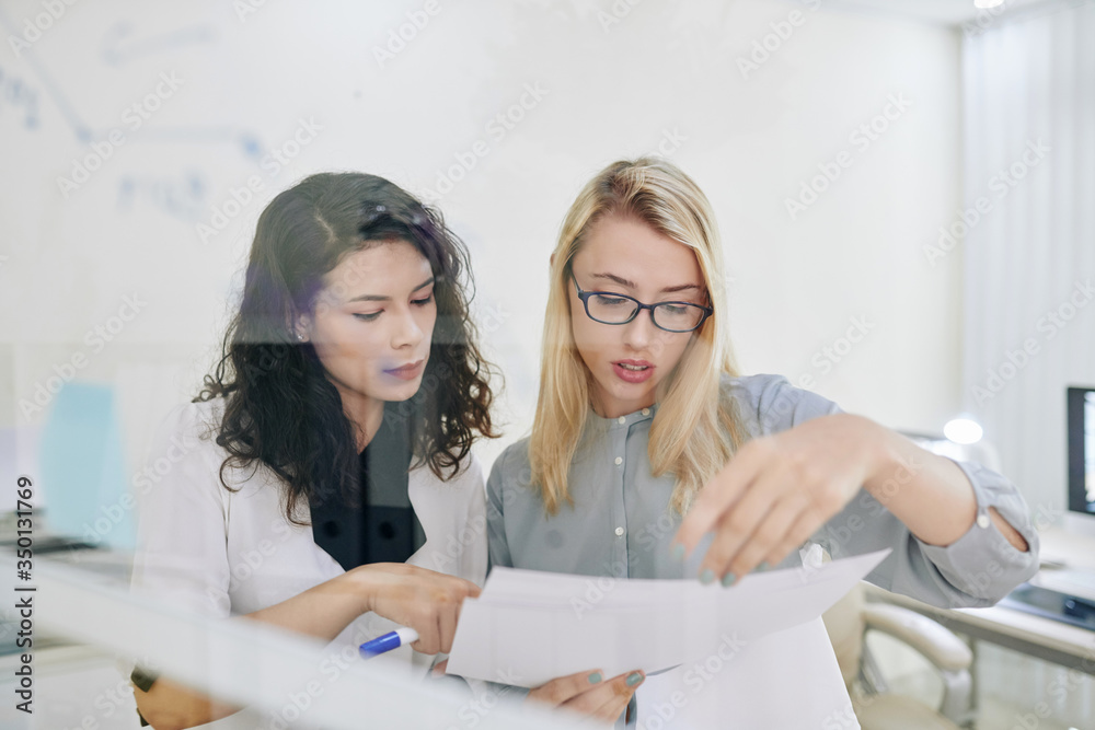 Serious young businesswomen reading and discussing documents at meeting Serious young businesswomen reading and discussing documents at meeting