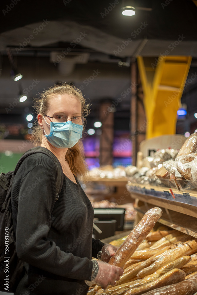 A young woman in a blue medical mask and transparent gloves buys bread in a supermarket. A woman is wearing a black sweater. Backpack. Woman with glasses. Covid-19. A young woman in a blue medical mask and transparent gloves buys bread in a supermarket. A woman is wearing a black sweater. Backpack. Woman with glasses. Covid-19.