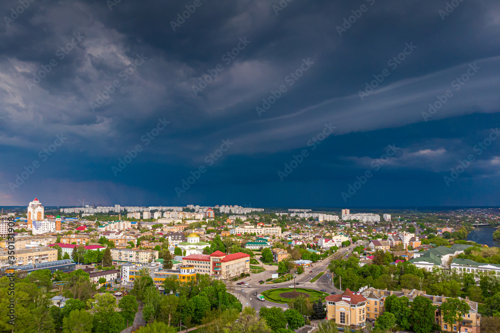 Beautiful dark blue thundercloud over the city. Top view of the city. Aerial photography. Houses, streets, green trees and parks. Cars are driving along the avenues.