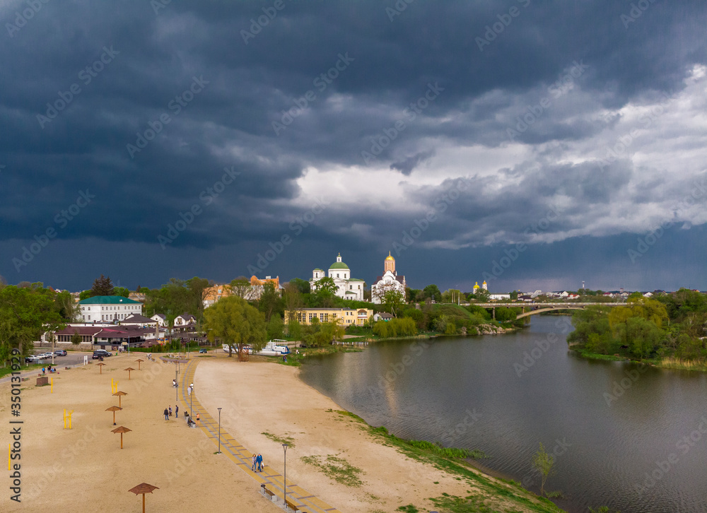 Beautiful dark blue thundercloud over the city. Top view of the city, churches, bridge, river. Aerial photography. The central beach of the city. People walk along the river. Beautiful dark blue thundercloud over the city. Top view of the city, churches, bridge, river. Aerial photography. The central beach of the city. People walk along the river.