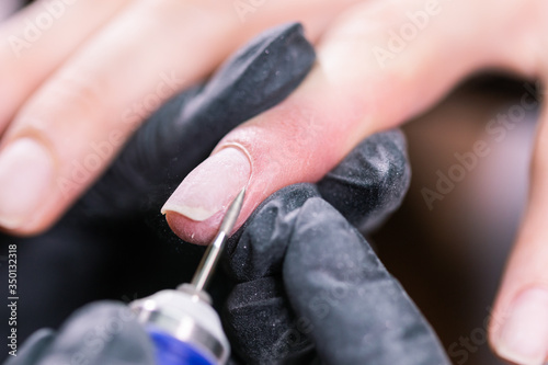 Hardware manicure in a beauty salon. Female manicurist is applying electric nail file drill to manicure on female fingers. Mechanical manicure close-up. Concept body care.