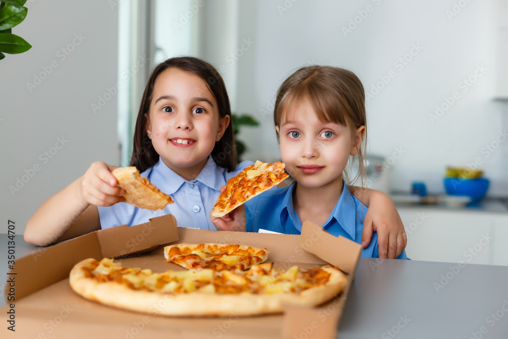 Two happy little child girl friends eating pizza slices.