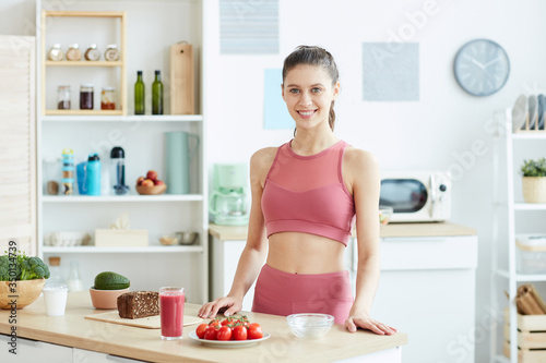 Waist up portrait of sportive young woman cooking healthy food in kitchen interior and smiling at camera, copy space
