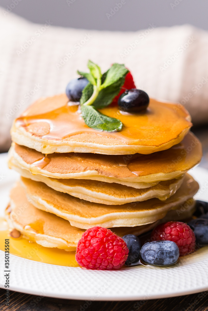 Pile of pancakes with blueberries and raspberries and maple syrup for breakfast on wooden table.