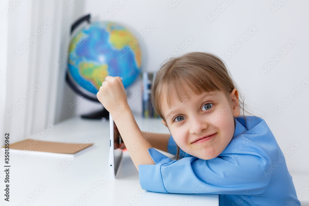 Cute little girl is sitting at table with her laptop and studying online Cute little girl is sitting at table with her laptop and studying online