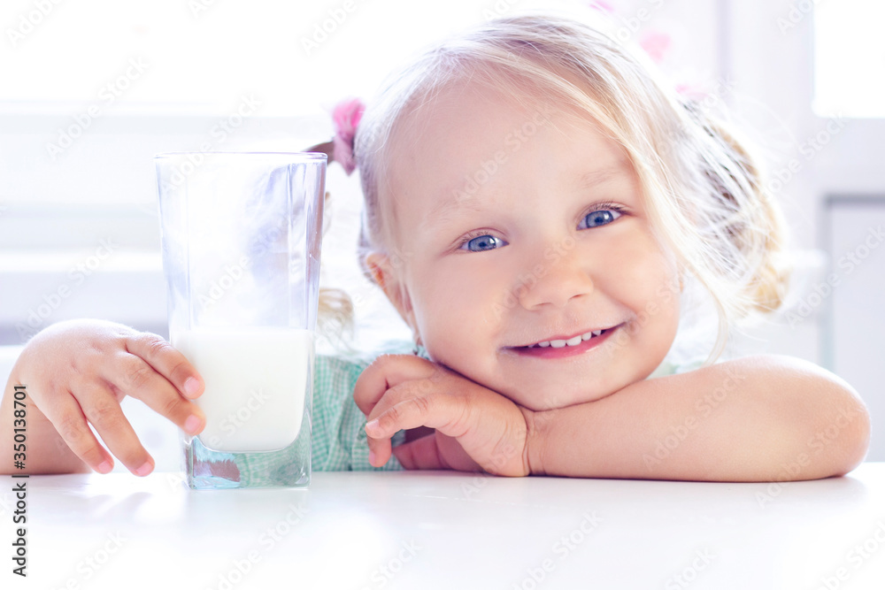 blonde girl smiles and drinks milk. light background. blonde girl smiles and drinks milk. light background.