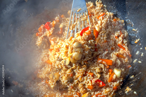 A delicious Uzbek pilaf with garlic and spices in a cauldron is cooked outdoors.
