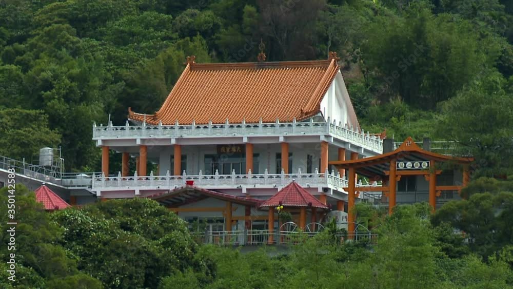 Ornate architecture and pagoda style roofs of traditional temple construction in Taiwan. Lush green mountain landscape in background with brightly colored building. Zoom out. Ornate architecture and pagoda style roofs of traditional temple construction in Taiwan. Lush green mountain landscape in background with brightly colored building. Zoom out.