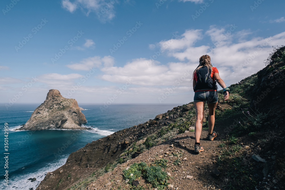 Woman runs cross country on a path in mountain path at Canary Island. Ocean view