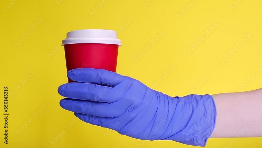 male hand courier wearing medical gloves holding paper cup coffee for take away isolated on yellow background. contactless delivery service in quarantine coronavirus pandemic. volunteer make donation male hand courier wearing medical gloves holding paper cup coffee for take away isolated on yellow background. contactless delivery service in quarantine coronavirus pandemic. volunteer make donation