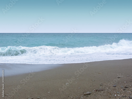 Sea coast, waves with foam, a beach with dark sand.
