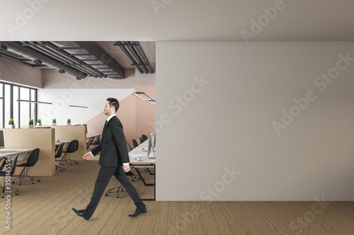 Businessman walking in office with blank wall.