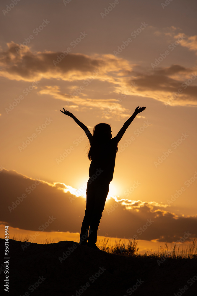Silhouettes of girls with hands up in the field on a sunset background.