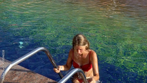 Summer season for girl going out of swimming pool holding for rails of ladder. Slow motion.