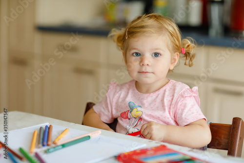 Cute adorable baby girl learning painting with pencils. Little toddler child drawing at home, using colorful felt tip pens. Healthy happy daughter experimenting with colors at home or nursery.