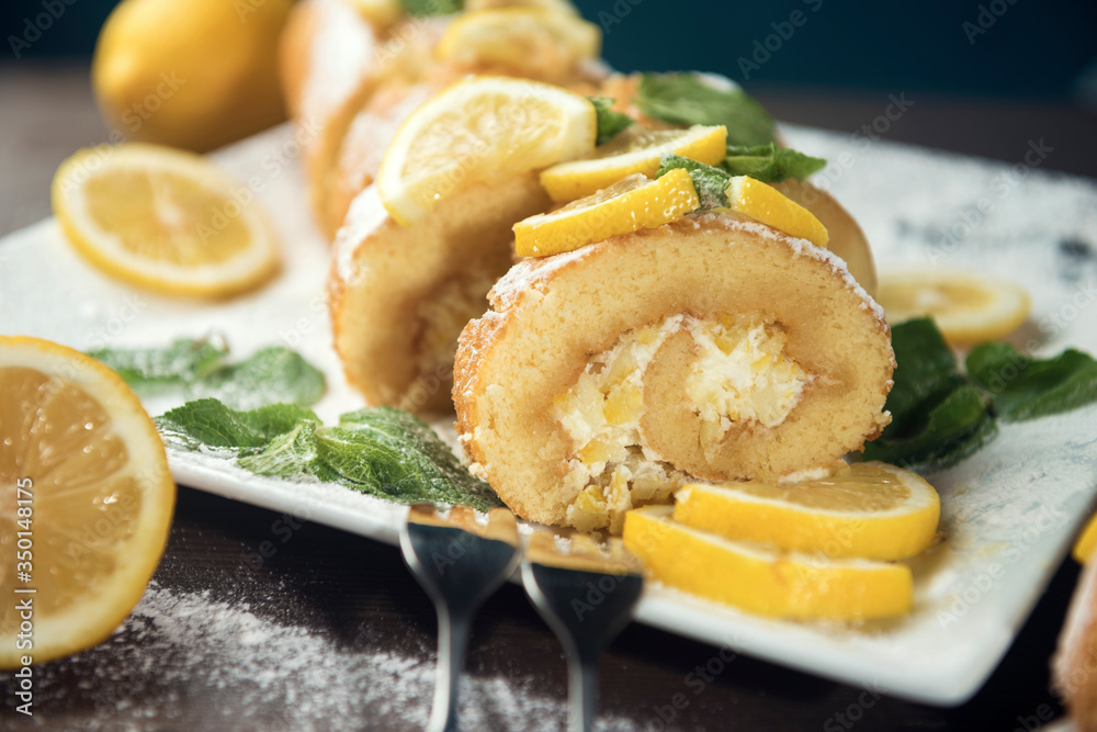 Lemon roll cake decorated with slices of lemon fruit and leaves of mint