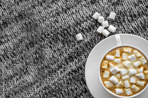 A Cup of coffee with marshmallows on a gray background. Next to the Cup are some marshmallows