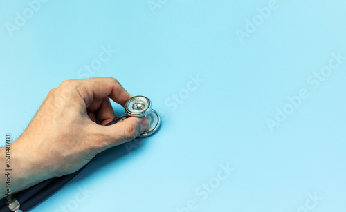 Doctors Hand Holding up a Stethoscope over blue background