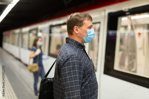 Man in protective medical mask is looking on railway and waiting train on platform in the underground