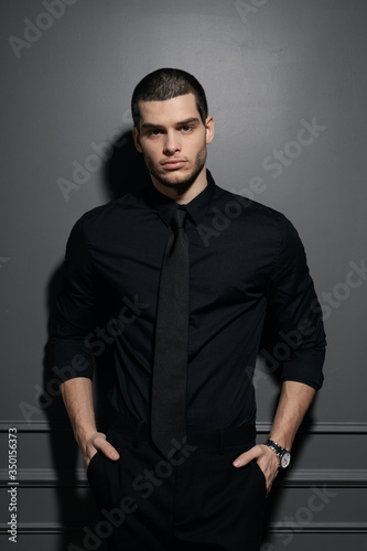 Young handsome businessman in black shirt. Confident young businessman posing on gray background
