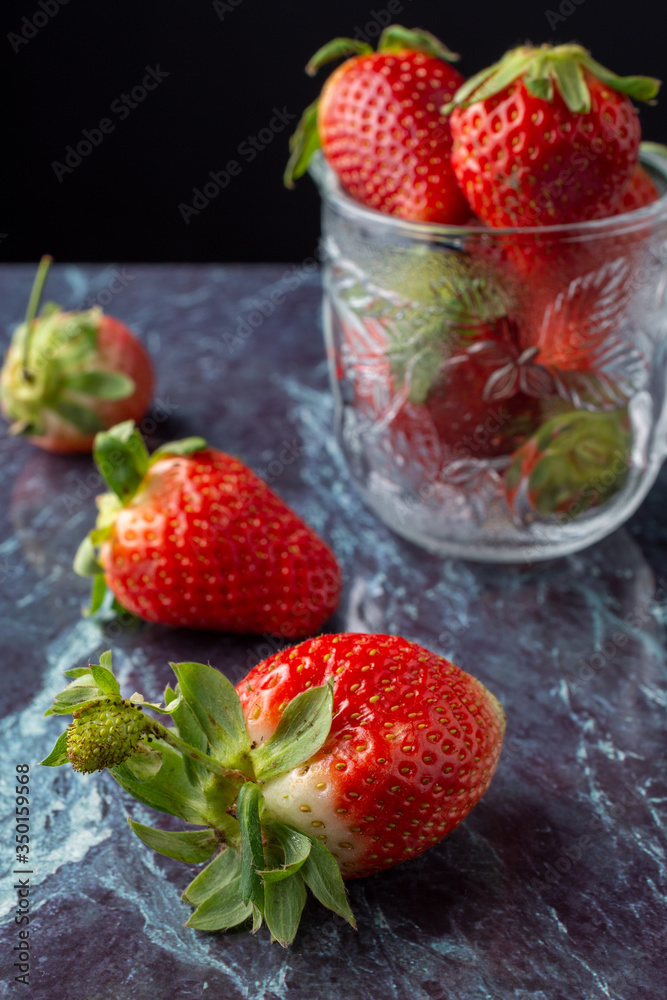 Close-up of strawberries on blue marble and glass jar, with selective focus, vertical Close-up of strawberries on blue marble and glass jar, with selective focus, vertical