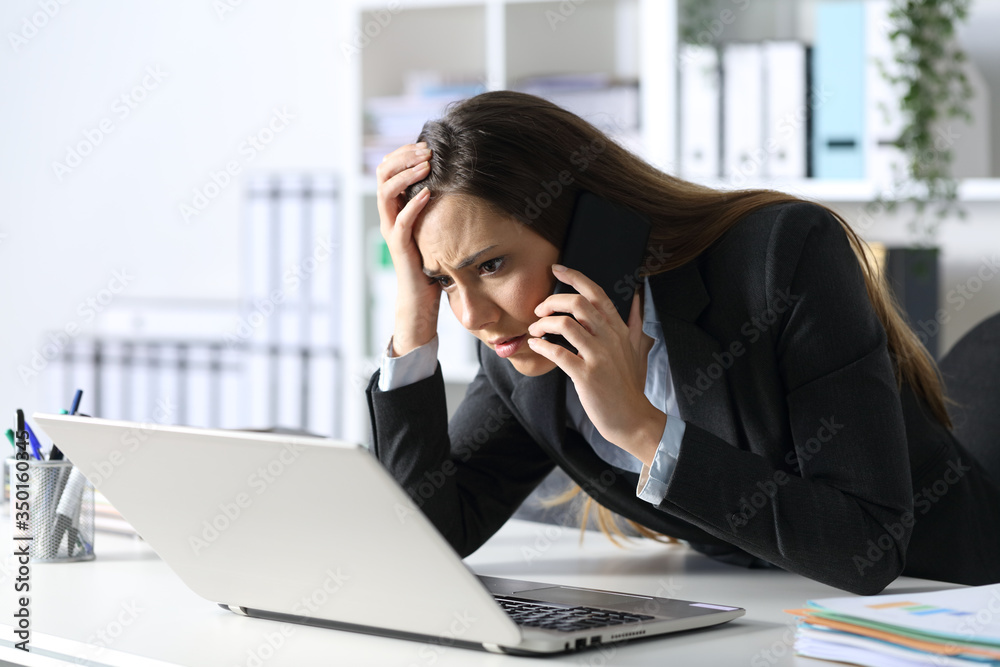 Sad executive calling on phone reading on laptop at office Sad executive calling on phone reading on laptop at office