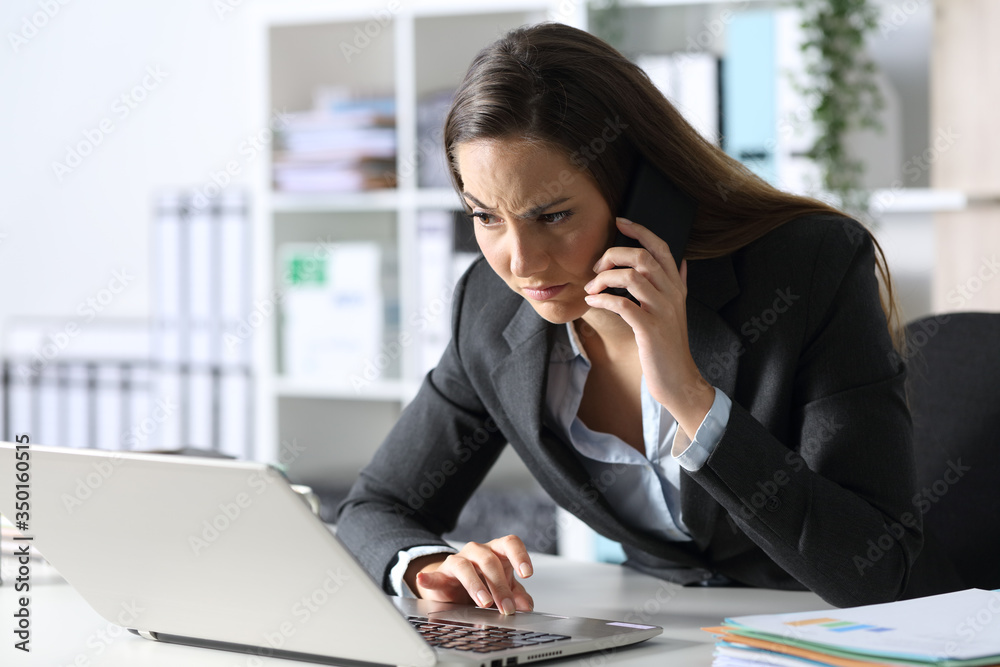Suspicious executive calling on phone looking laptop at office Suspicious executive calling on phone looking laptop at office