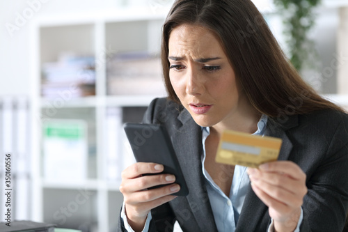 Worried executive paying on phone with card at office