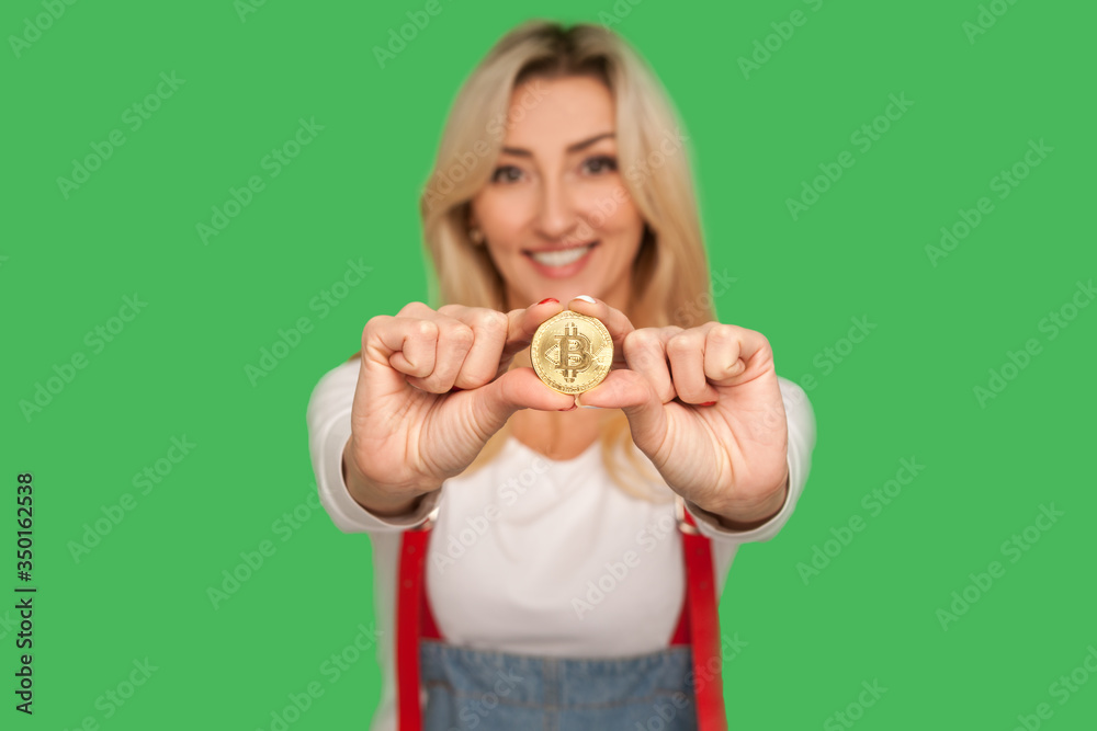 Look at digital money! Portrait of happy adult blond woman with charming smile holding golden bitcoin, showing btc coin and expressing optimism, joy. indoor studio shot isolated on green background Look at digital money! Portrait of happy adult blond woman with charming smile holding golden bitcoin, showing btc coin and expressing optimism, joy. indoor studio shot isolated on green background