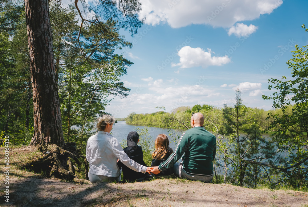 Family of four sit on the bank of the river in the spring forest Family of four sit on the bank of the river in the spring forest