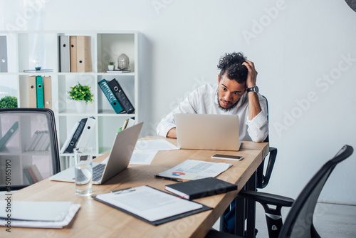 Selective focus of african american businessman using laptop near papers and smartphone on table in office