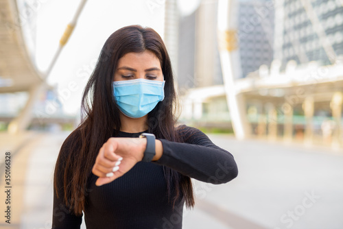 Young Indian woman with mask checking the time at the skywalk bridge photo