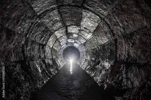 Round drainage concrete tunnel with water built with formwork. With light at the end. Underground river hidden in tube.