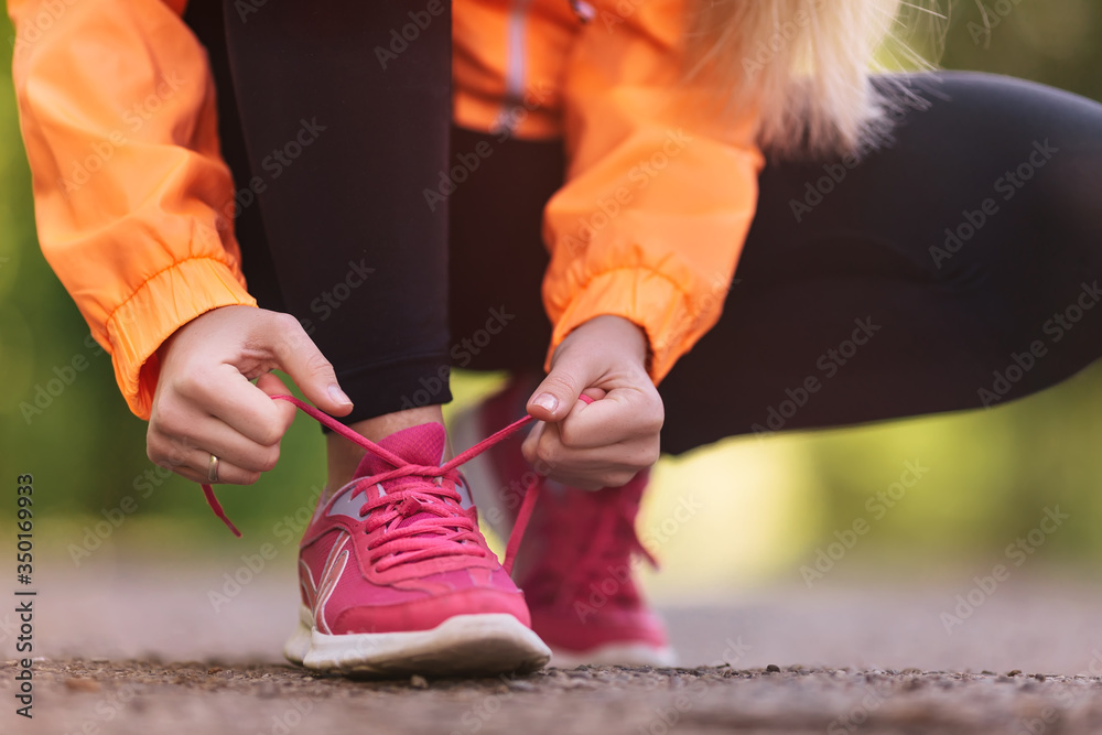 Close up of girl lacing running shoes for jogging outdoors in th