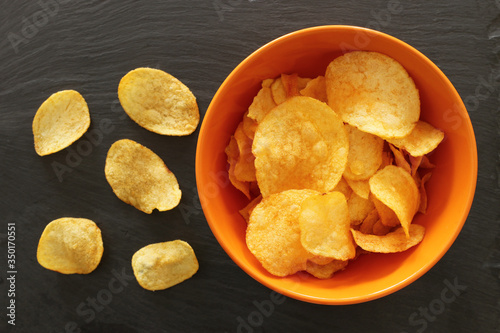 Top view image of potato chips slices in the bowl over slate stone background