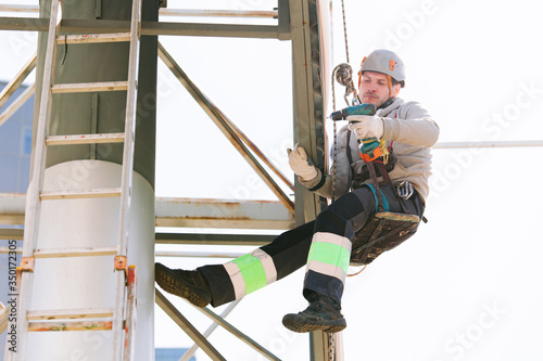 Industrial climber in helmet and overall working on height. Risky job. Professional worker