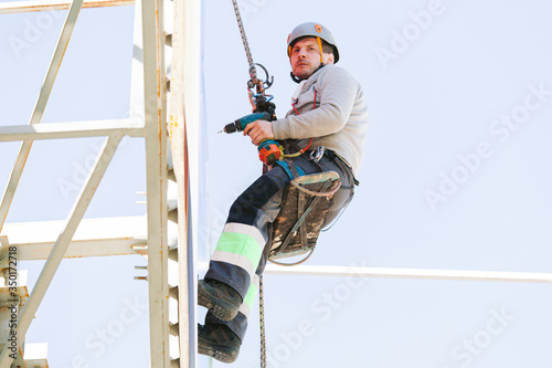 Industrial climber in helmet and overall working on height. Risky job. Professional worker