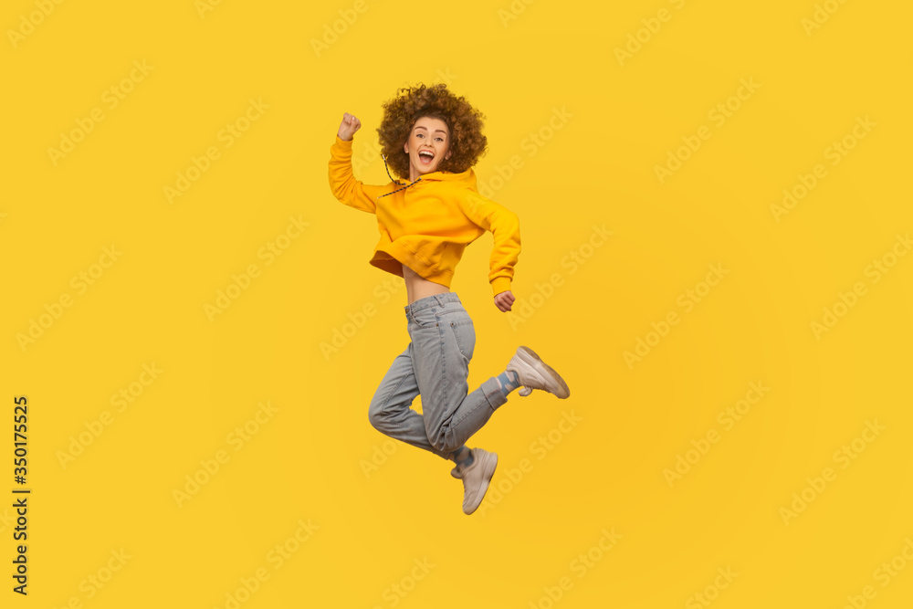 Portrait of enthusiastic joyful curly-haired girl in urban style hoodie and jeans jumping high in air, flying and shouting with amazed happy expression, celebrating success. studio shot isolated Portrait of enthusiastic joyful curly-haired girl in urban style hoodie and jeans jumping high in air, flying and shouting with amazed happy expression, celebrating success. studio shot isolated