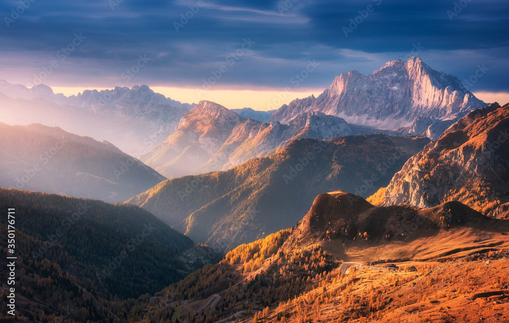 Beautiful mountains at sunset in autumn in Dolomites, Italy. Landscape with rocks, sunbeams, forest, hills with orange grass and trees, colorful sky. Scenery with mountain valley in fog in fall
