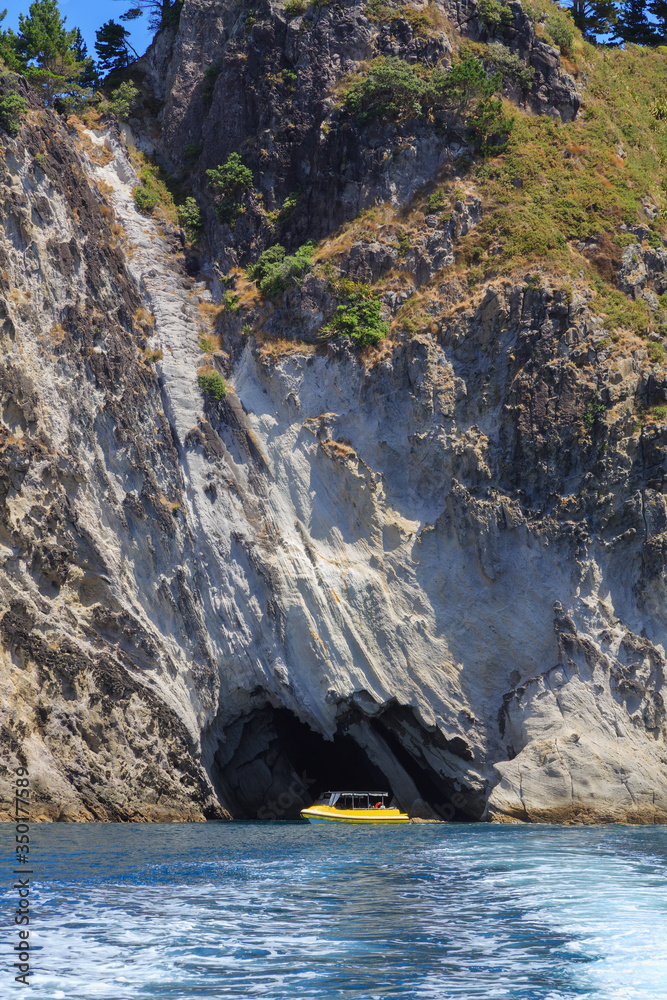 A tour boat outside a sea cave in the steep coastal cliffs near Hahei on the Coromandel Peninsula, New Zealand