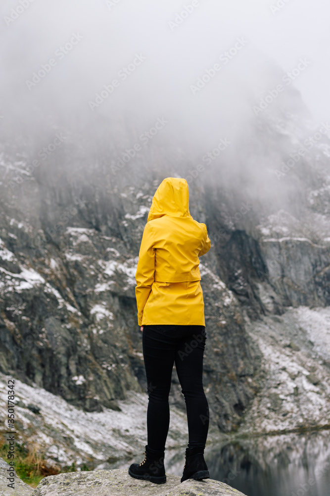 Obraz premium Journey to the mountains. A young woman in a yellow jacket looks at a mountain range covered in snow. A girl stands with her back turned.