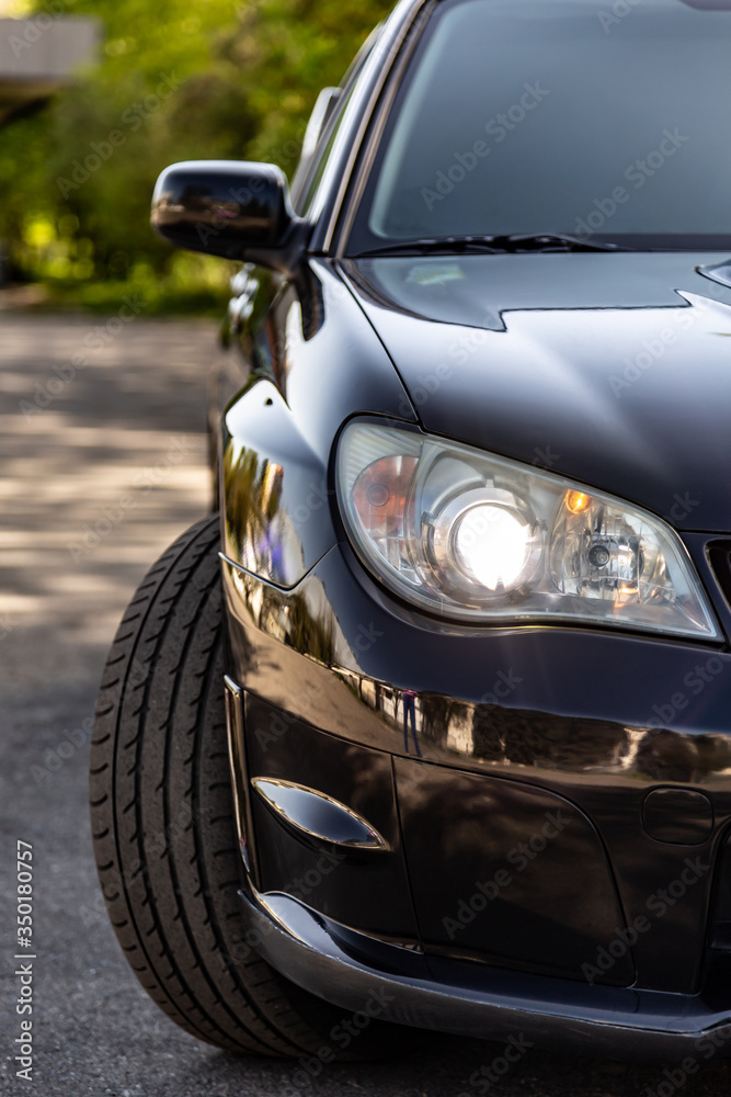The black car. Front view half of the car - headlight and a turned wheel. Summer sunny day. Vertical orientation.