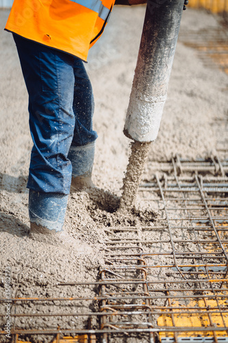 Worker wearing safety equipment using cement pump and pouring concrete slab