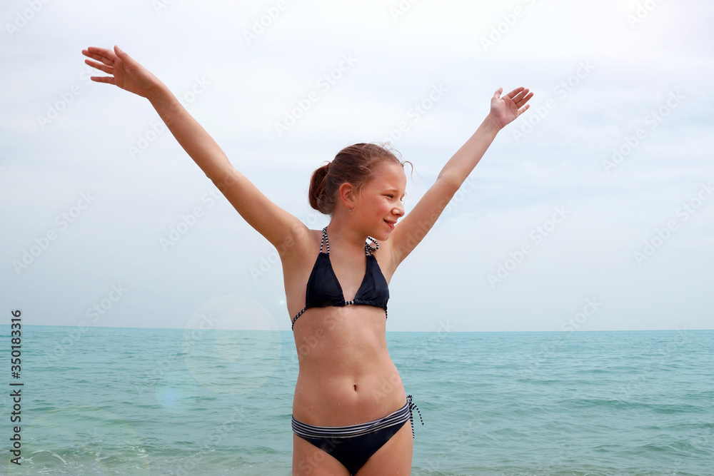 girl in a swimsuit at sea rejoices with hands up
